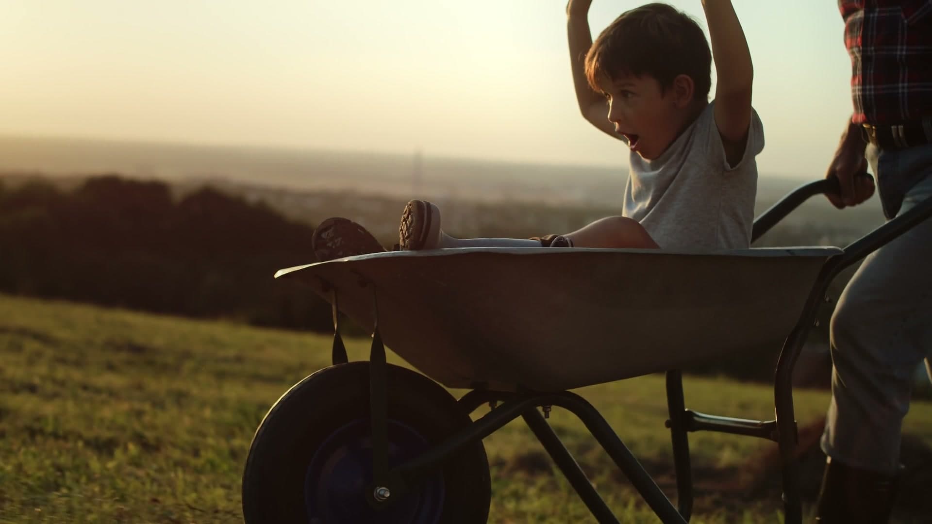 A boy rides a wheelbarrow at golden hour